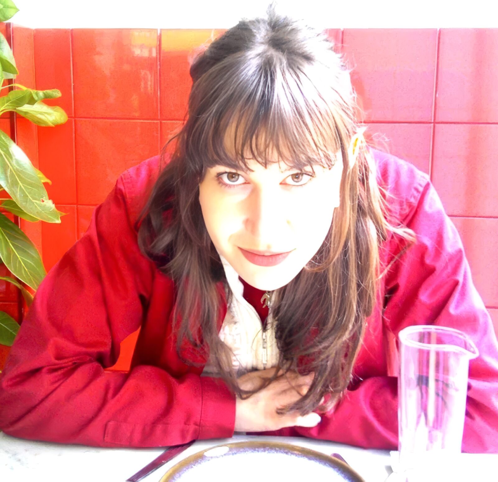 The artist leaning over a café table, in a red jacket against a red tiled wall